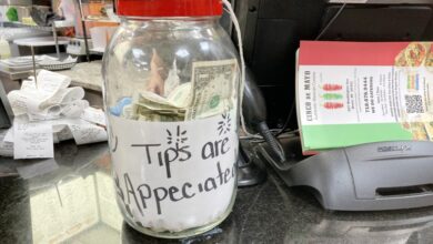 A clear jar filled with money and a label that appears to be made of paper sitting on a table in a restaurant in the Bronx, NY.