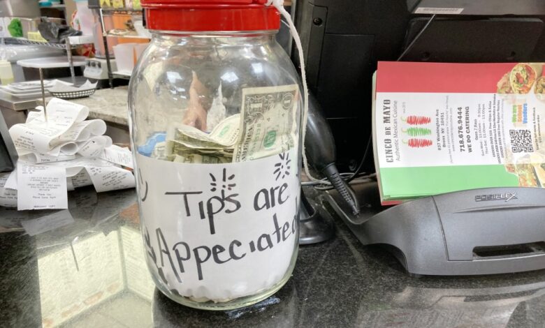 A clear jar filled with money and a label that appears to be made of paper sitting on a table in a restaurant in the Bronx, NY.