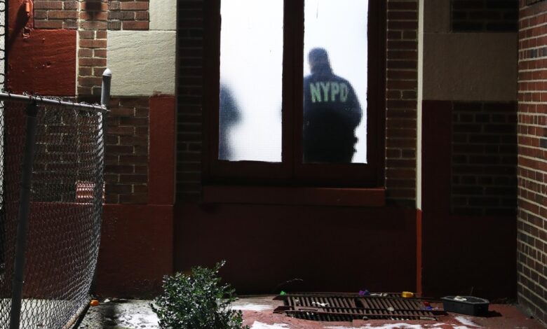 A NYPD officer stands inside the window of a Brooklyn apartment building with his back to the fogged glass