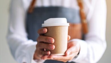 A waitress serving a paper cup of hot coffee in a cafe.