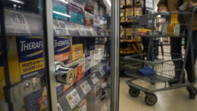 Locked pharmaceuticals in a glass cabinet at a store with a shopping cart visible in the background.