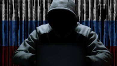 A hacker sitting with a hood against a backdrop of binary code.