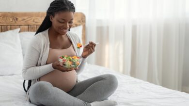 Happy pregnant African American woman sitting in bed, enjoying a fresh vegetable salad