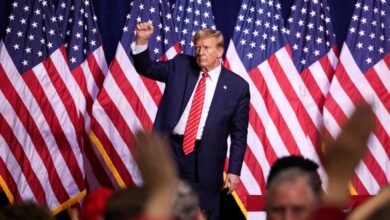 Former U.S. President Donald Trump reacting during a campaign rally, standing in front of a crowd of flags at the Forum River Center in Rome, Georgia.