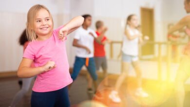Positive girl exercising in group of classmates during dance class at school