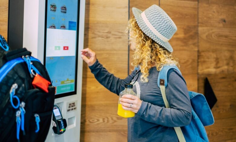 Woman make food order in modern display at fast food restaurant - self-service panel technology and people in travel lifestyle taking hamburger to eat