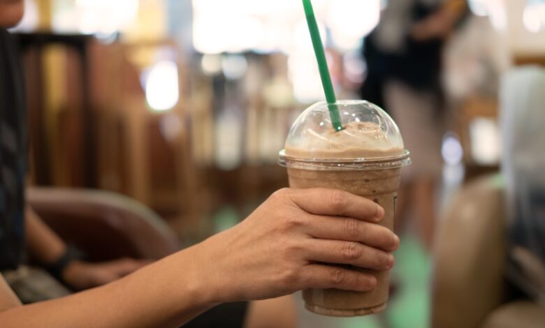 Woman holding a slimmed down plastic glass of iced coffee with milk and a straw