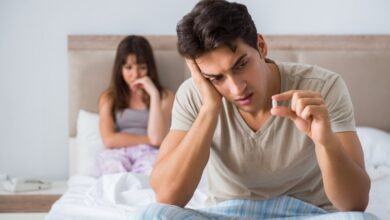 A man holding a pill for erectile dysfunction with a woman sitting in the background