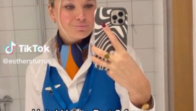 A flight attendant named Esther Sturrus taking a mirror selfie while demonstrating her hotel hack of rolling a water bottle under the bed for safety