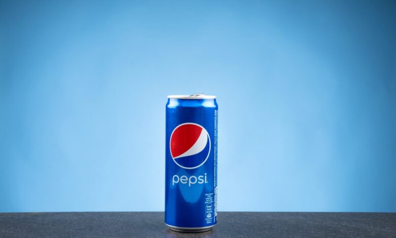 A can of Pepsi on a flat surface against a blue backdrop.