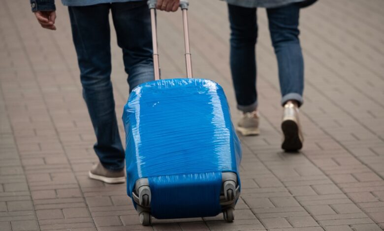 A man carries a suitcase wrapped in blue film