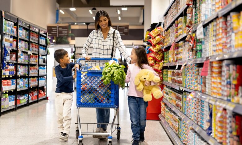 Happy Latin American woman grocery shopping at the supermarket with her children and smiling while pushing a shopping cart