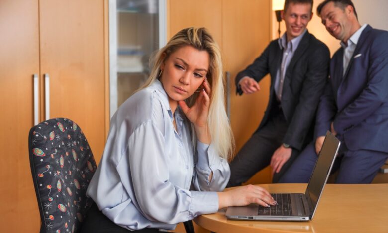 Two men making fool of a woman sitting at her laptop and trying to work.