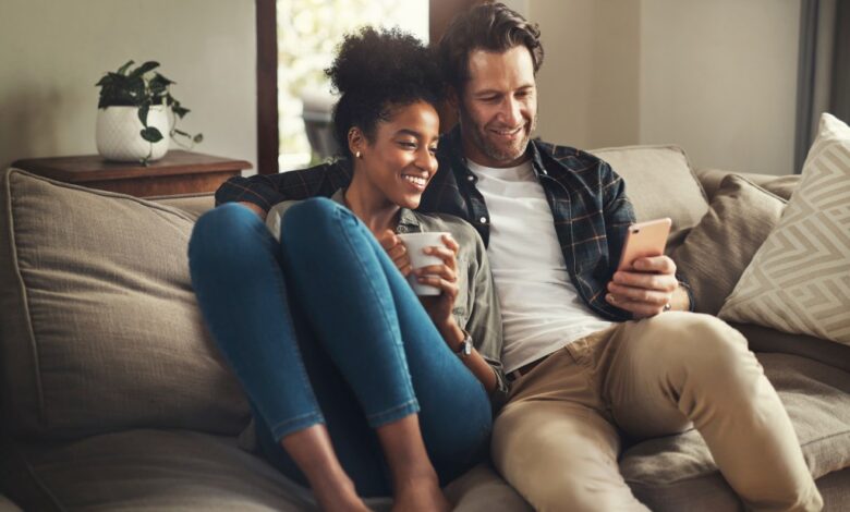 Happy young couple sitting on a couch in their living room, browsing on a digital tablet