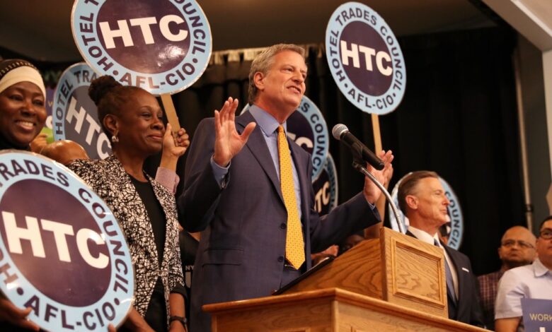 Bill de Blasio standing at a podium at a rally as the Hotel and Motel Trades Council union endorses him, with Chirlane McCray in the audience.