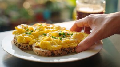 A hand holding a plate of soft scrambled eggs on toast