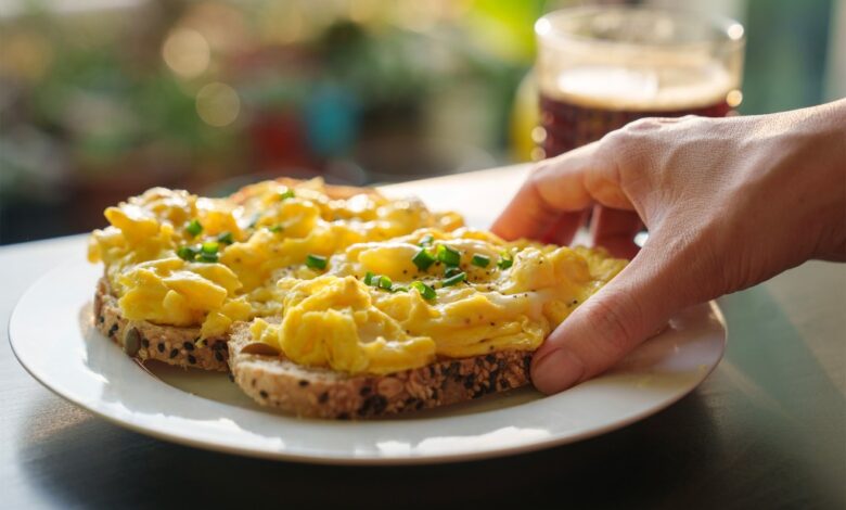 A hand holding a plate of soft scrambled eggs on toast