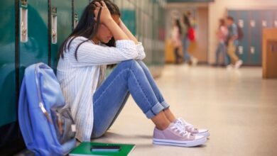 Frustrated Asian teenage girl sitting with head in hands in a brightly illuminated school corridor against metallic lockers