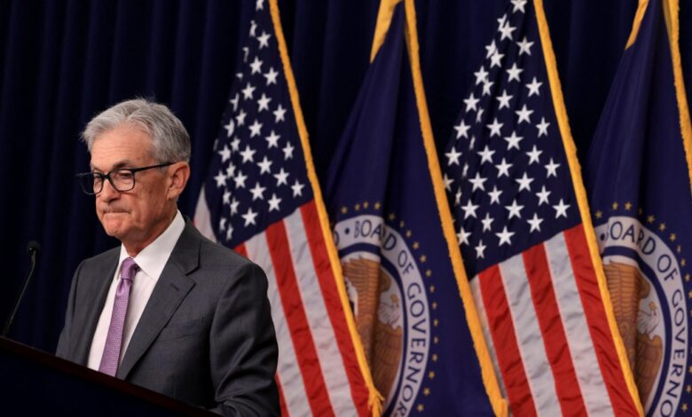 Federal Reserve Chair Jerome Powell conducting a press conference on interest rate policy at a podium with US flags behind him