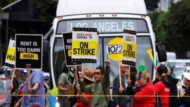 Hotel workers holding signs as they march and protest for their rights in Los Angeles, while a bus driver waits to cross the road, captured on October 25, 2023.