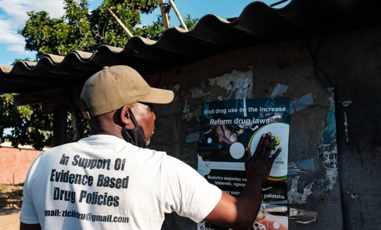 an outreach officer with Zimbabwe Civil Liberties and Drugs Network, sticks a poster warning of the dangers of using crystal meth to a wall in Glen View township in Harare, Zimbabwe.