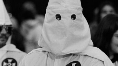 A person wearing a white hooded robe, identified as a member of the Ku Klux Klan