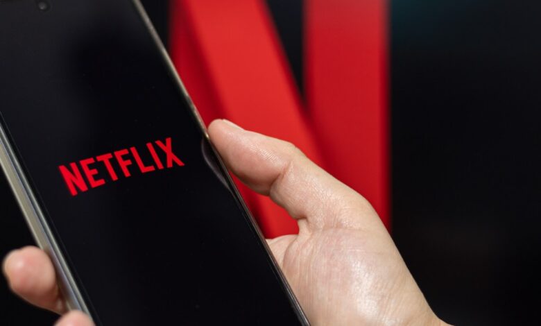 A person opening Netflix on their phone with the Netflix photo in the background.