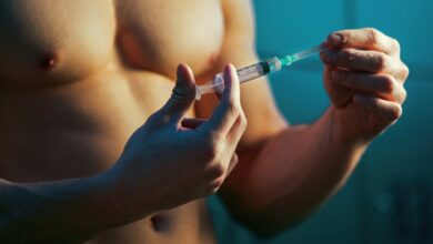 Close-up view of a male bodybuilder preparing to inject performance-enhancing drugs in a locker room before training.