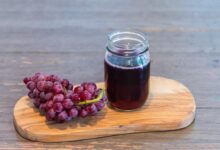 Grape drink in glass jar on a cutting board, next to a bunch of grapes on a rustic wood table