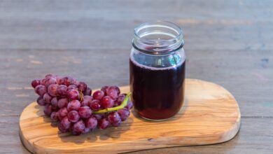 Grape drink in glass jar on a cutting board, next to a bunch of grapes on a rustic wood table