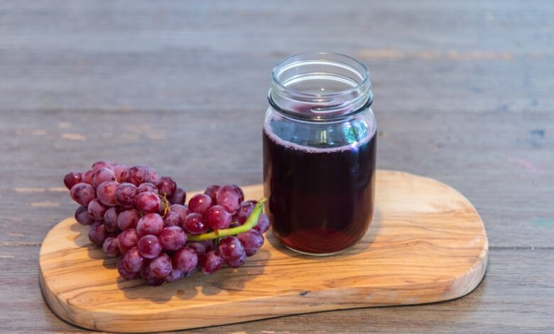 Grape drink in glass jar on a cutting board, next to a bunch of grapes on a rustic wood table