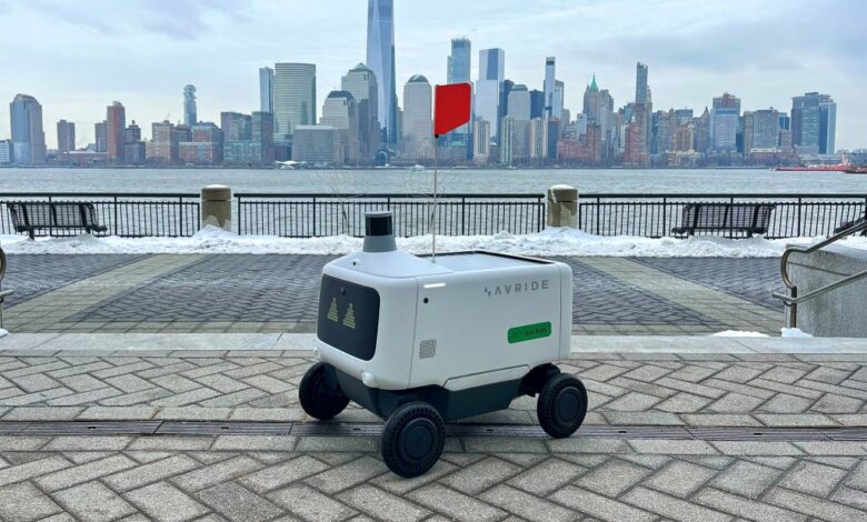 Autonomous delivery robot on wheels with a cityscape in the background, part of Uber's expanded food delivery service on the East Coast.