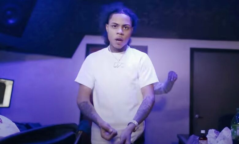 A photo of drill rapper Kay Flock wearing a white t-shirt, silver necklace and with a large watch