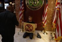 Climate activist David Huebner from Extinction Rebellion kneeling in front of a 'USA' sprayed over the presidential placard inside NYC Trump Tower.