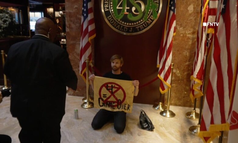 Climate activist David Huebner from Extinction Rebellion kneeling in front of a 'USA' sprayed over the presidential placard inside NYC Trump Tower.