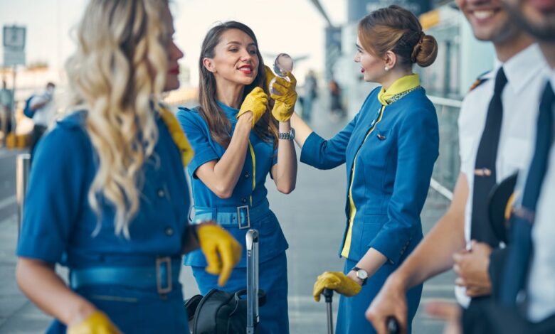 Flight attendant smiling while looking in the mirror, with fellow stewardesses and pilots waiting for flight in the background