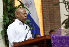 New York City Mayor Eric Adams speaking at a podium during a mass in Santo Domingo for the victims of a roof collapse