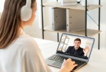 Male teacher giving encouraging OK gesture to female student via video chat on laptop for online education at a modern light workplace