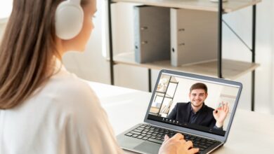 Male teacher giving encouraging OK gesture to female student via video chat on laptop for online education at a modern light workplace