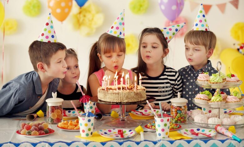 Group of joyful children blowing out candles on a birthday cake at a party