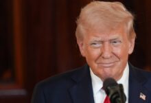 Trump in a red tie and navy suit speaks at the White House