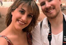 Couple smiling for a selfie in front of a cityscape.