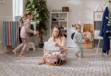 A mother sorts laundry in a basket while her two young daughters play nearby.