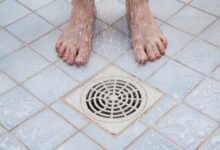 Bare feet being showered over a drain.