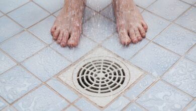 Bare feet being showered over a drain.