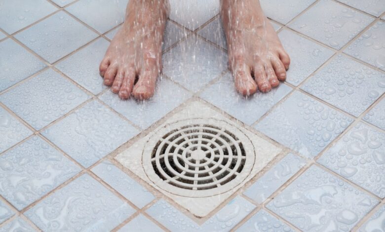 Bare feet being showered over a drain.