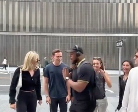 A man in a black shirt and hat stopping a group of young people on a New York City street, vocally criticizing them.