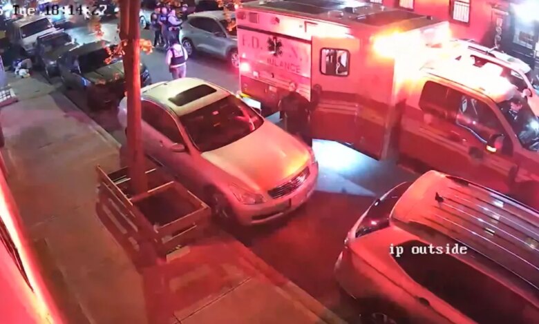 An ambulance and police cars on a street with officers and people standing near the vehicles.