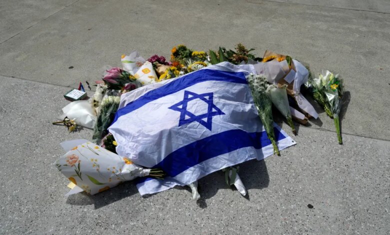 An Israeli flag laid on the ground amongst flowers, tributes, and a small notebook with pens.