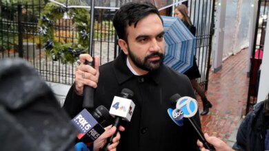Zohran Mamdani speaks to reporters while holding an umbrella in the rain.